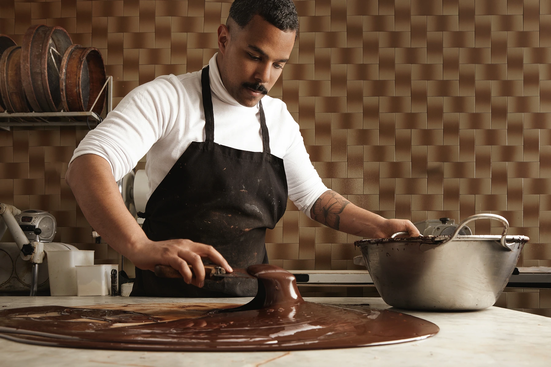 black-man-professional-chief-collects-tasty-melted-chocolate-from-vintage-marble-table-big-steel-pot-his-artisan-rustic-kitchen-with-industrial-retro-machines 1