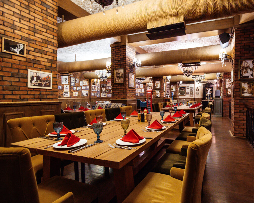 a restaurant hall with red brick walls wooden tables and pipes in the ceiling